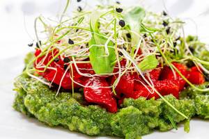 Nahaufnahme eines Salats mit Zwiebelsprossen, roter Paprika und grünem Püree aus Gemüse und Kräutern