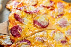 Nahaufnahme eines Stückes heißer Pizza mit Käse und Wurst