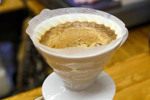 Nahaufnahme Filterkaffee in Aufgusstrichter aus Keramik mit Filterpapier vor Holzhintergrund