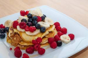 Nahaufnahme Food Foto von Protein Pfannenkuchen mit Himbeeren, Blaubeeren, Banane und Honig auf weißem Teller