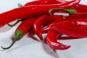 Nahaufnahme frische, leuchtend rote Chilis für scharfe Gerichte auf weißem Holztisch