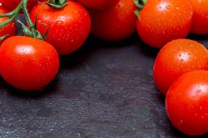 Nahaufnahme frische, leuchtend rote Tomaten mit Tautropfen auf schwarzem Hintergrund