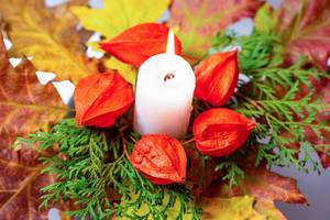 Nahaufnahme - Leuchtenede Kerze mit Physalis, Tannenzweigen und bunten Herbstblättern