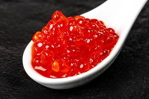 Nahaufnahme: roter Kaviar in weißem Löffel auf schwarzem Hintergrund