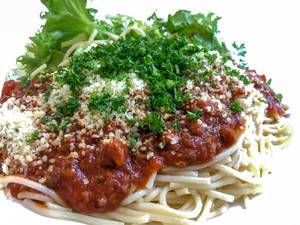 Nahaufnahme Spaghetti mit Tomatensoße, geriebenem Käse, Kräutern und Salatblättern