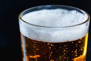 Nahaufnahme von Bier in Glas mit leichtem Bierschaum vor dunklem Hintergrund