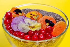 Nahaufnahme von einem gesunden Frühstück: Haferflocken mit Beeren, Chiasamen und essbaren Blumen