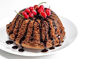 Nahaufnahme von einem Schoko-Kuchen mit roten Beeren auf einem weißem Teller vor weißem Hintergrund