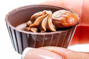 Nahaufnahme von einem Schokoladenbonbon mit Mandel und Creme in einer Frauenhand