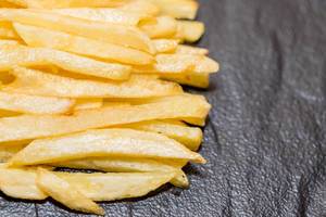 Nahaufnahme von frisch frittierten Pommes Frites auf schwarzem Hintergrund