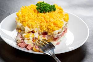 Nahaufnahme von gesundem Salat aus Schinken, Kartoffeln, Eiern und Mayonnaise auf weißem Teller mit einer Gabel