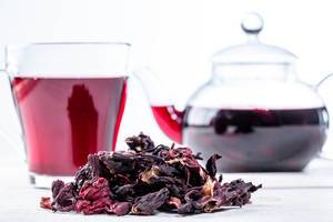 Nahaufnahme von getrocknetem Hibiskus und aufgebrühtem roten Tee in einem Glas und einer gläsernen Teekanne