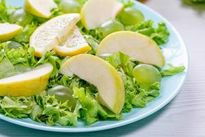 Nahaufnahme von grünem Salat mit Apfelstücken und Weintrauben auf einem blauen Teller