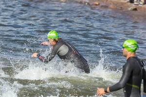 Nahaufnahme von Ironman-Schwimmsportlern, die für die erste Triathlondisziplin in den See springen und Wasserspritzer erzeugen