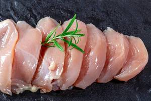 Nahaufnahme von rohem, zu Filets geschnittenem Hühnerfleisch mit Rosmarin