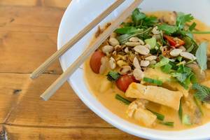 Nahaufnahme von veganem, vietnamesischem Essen: Fleischloses Bio-Tofu-Curry mit Nüssen, Kräutern und Essstäbchen, auf einem Holztisch