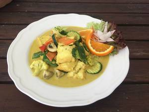 Nahaufnahme zeigt Mittagessen für eine vegane Ernährung, mit Gemüse, Pilzen und Orange in einer Curry Kurkuma Sauce, auf einem weißen Teller