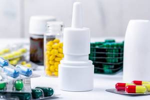 Nasenspray mit verschiedenen Tabletten und bunten Kapseln im Hintergrund