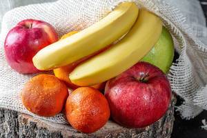 Nasse Äpfel, Bananen, Mandarinen und Orangen auf einem Leinentuch auf einem Baumstamm