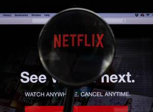 Netflix-Logo am PC-Monitor, durch eine Lupe fotografiert