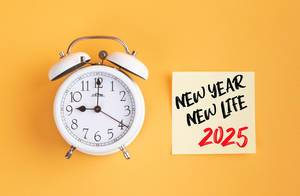 Neue Anfänge: Wecker und ein Zettel mit ‘New year - New life 2025’ Text vor gelbem Hintergrund