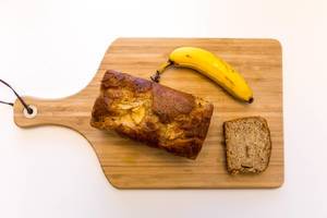 Neue Werte Banana bread with apple and cinnamon and a raw banana on a cutting board on a white background