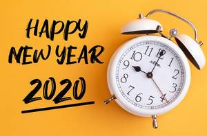 Neues Jahr: Weißer Wecker mit dem Text ‘Happy new year 2020’ vor gelbem Hintergrund