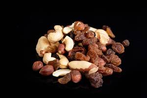 Nuss-Mischung aus Cashews, Haselnüssen und brasilianischen Nüssen mit Rosinen vor schwarz