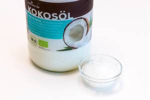 Nutriverde Kokosöl in einer Flasche und kleiner Glasschale, auf einem weißen Tisch