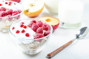 Oatmeal porridge with raspberries and red currant in bowl on white table
