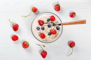 Oatmeal with blueberries and strawberries with spoon on white wooden background. Top view