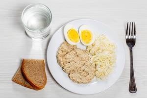 Oatmeal with fresh cabbage salad and boiled eggs on a white table with black bread and a glass of water