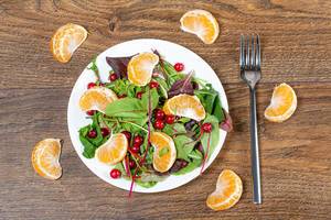 Obene Aufnahme von einem leichten Salat aus Spinatblättern, Mandarinen und Moosbeeren