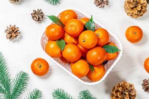 Obene Aufnahme von frischen Mandarinen in einer weißen Schachtel mit Zapfen und Tannenzweigen