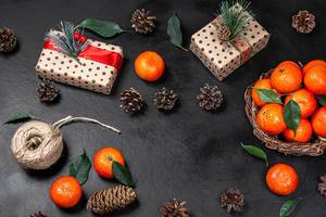 Obene Aufnahme von Weihnachstgeschenken mit Mandarinen und Zapfen auf einem schwarzen Tisch