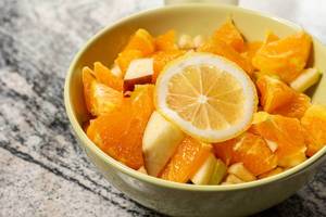 Obstsalat aus geschnittenen Orangen, Äpfeln dekoriert mit Zitronenscheibe in Schüssel