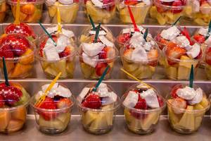 Obstsalat to go mit Erdbeeren, Melone und Kokosnuss im Plastikbecher mit Plastikgabel in der Markthalle La Boqueria in Barcelona, Spanien