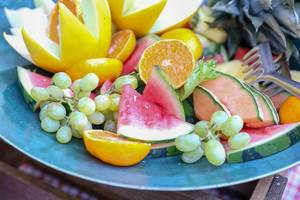 Obststeller mit grünen Weintrauben, Melone, Orange und Ananas
