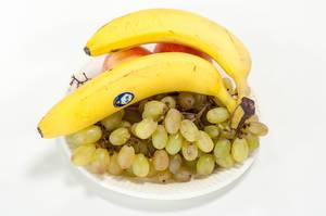 Obstteller mit Trauben, Bananen und Äpfeln vor weißem Hintergrund