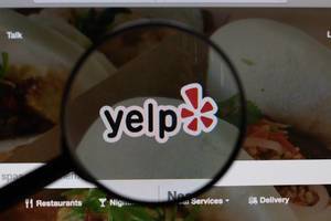 Offizielles "Yelp" Logo und Schriftzug, vergrößert durch ein Lupenglas dargestellt