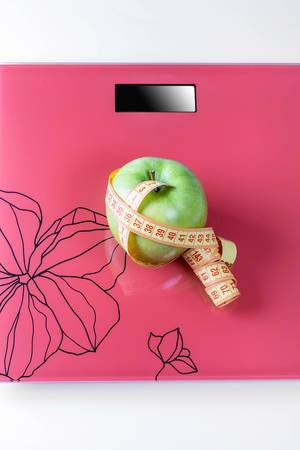 On the scales is a measuring tape and a green Apple-the concept of weight loss