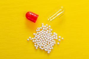 Open capsule and white drug granules on yellow background
