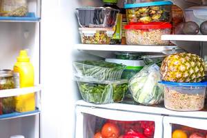 Open Fridge filled up with groceries such as Mustard, Lettuce, Beans, Pineapple, Tomatoes, Apple and Avocados