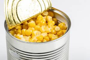 Open tin can with corn kernels on white background