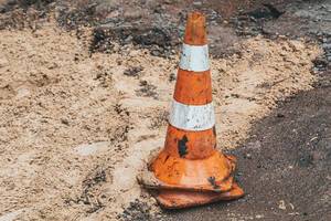 Orange and white striped cone on an asphalt pavement repair site