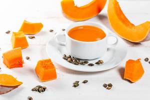 Orange Suppe des Kürbises mit Scheiben des frischen Kürbises und der Samen auf weißem hölzernem Hintergrund