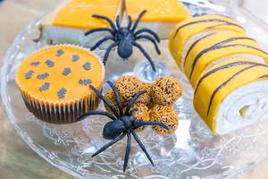 Orangefarbene Halloween Süßigkeiten mit Deko-Spinnen auf Glasteller