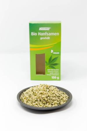 Organic vegan peeled hemp seeds on a plate in front of the packaging on white Background
