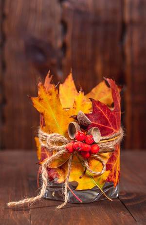 Original candle holder with autumn leaves and Rowan berries on wooden background
