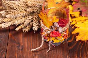 Original candlestick with autumn leaves and Rowan berries on a wooden background with wheat spikelets